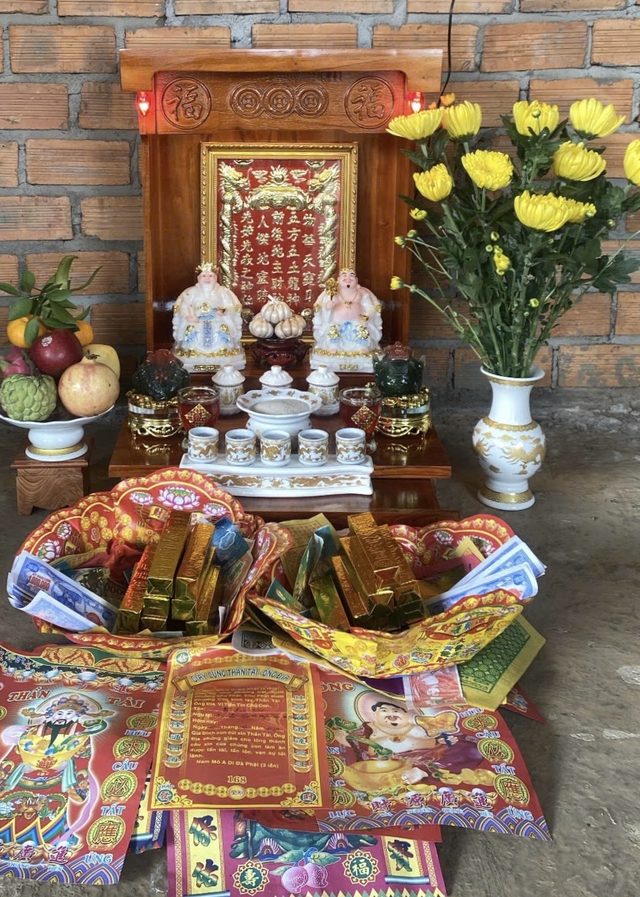Bàn thờ Thần Tài của khách dựa tường gạch, hoa cúc vàng và đồ cúng
